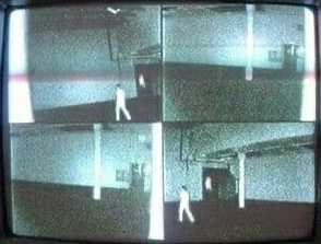 4분할 CCTV 모니터. 빈 공장 구역을 흰 옷의 인물이 걷고 있습니다